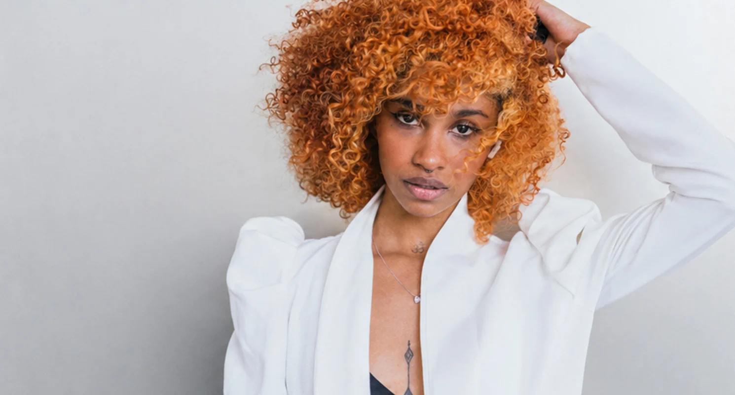 Model with a voluminous curly copper hairstyle and warm golden tones